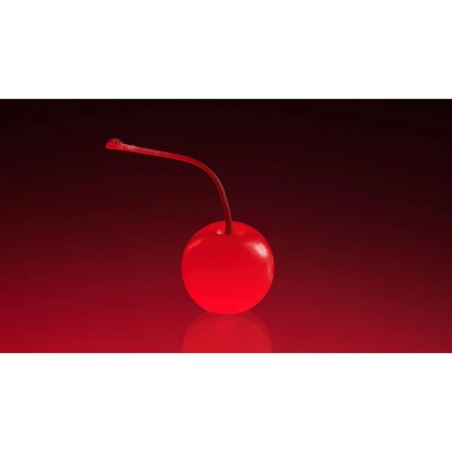 Close-up studio shot of a shiny red maraschino cherry with its stem against a dark red gradient background with a reflective surface.