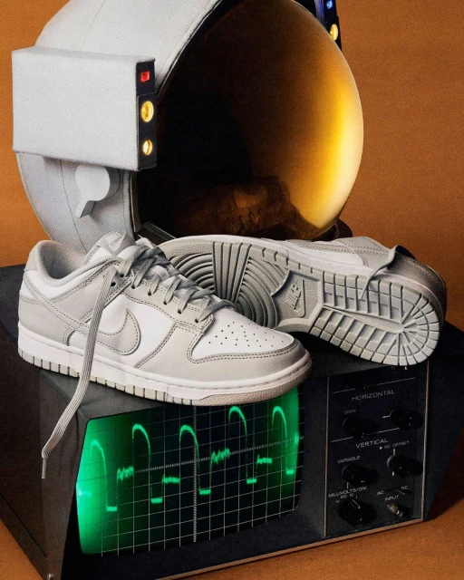 Close-up studio shot of white and gray Nike sneakers placed on a vintage television with a graphic display, next to an astronaut helmet.