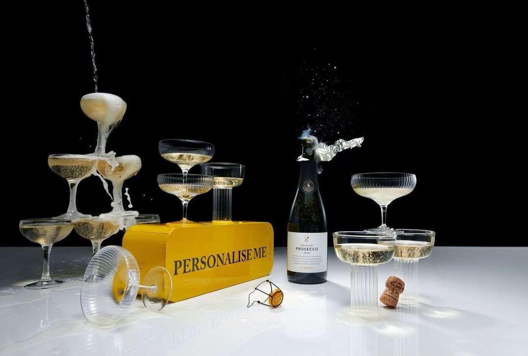 Champagne tower of glasses and a bottle of Prosecco with an exploding cork. Festive celebration on a white surface against black.