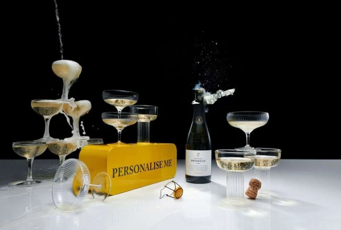 Champagne tower of glasses and a bottle of Prosecco with an exploding cork. Festive celebration on a white surface against black.