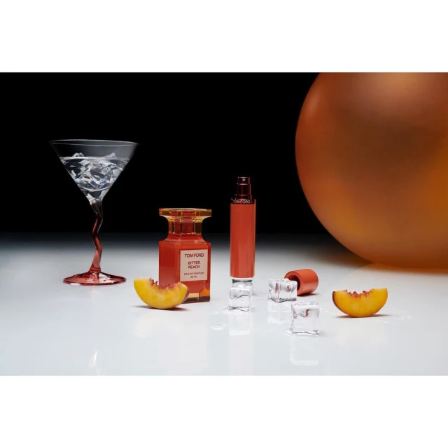 Tom Ford Bitter Peach perfume bottles with peach slices and ice cubes in an indoor product shot against black and white background.