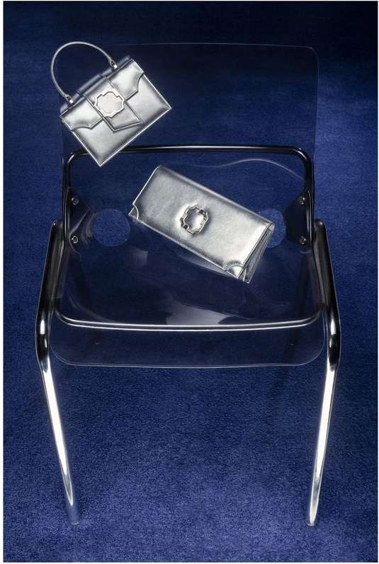 Silver handbags on a clear chair against a dark blue backdrop, offering a sleek and modern aesthetic for fashion accessory display.
