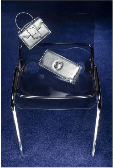 Silver handbags on a clear chair against a dark blue backdrop, offering a sleek and modern aesthetic for fashion accessory display.
