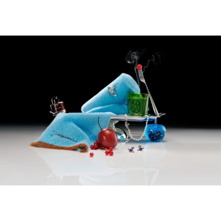 Still life composition featuring a blue fur accessory, candle, perfume bottle, cherry, and pearls against a black background.