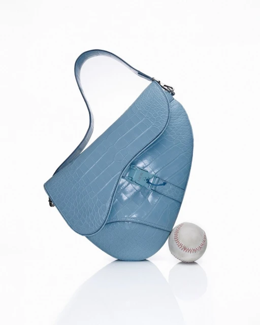 Light blue leather purse with crocodile skin texture on a white background with a baseball, studio lighting, and high-key tones.