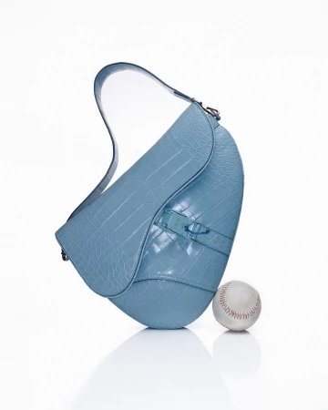 Light blue leather purse with crocodile skin texture on a white background with a baseball, studio lighting, and high-key tones.