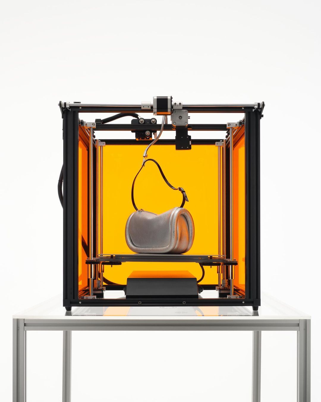 3D printer with a silver bag inside on a white table against a white background, showcasing technology and design.