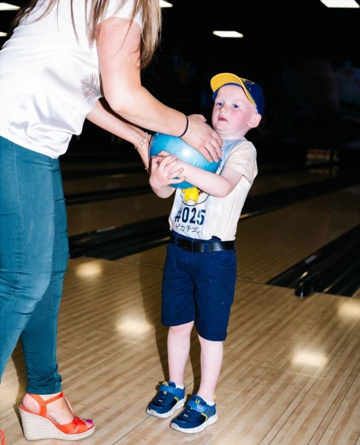 Young boy holding a bowling ball with help from adult at an indoor bowling alley with a wood lane surface and black pin dividers.