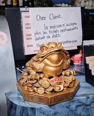 Golden money frog statue on a blue marble surface next to a sign in French, in an indoor setting with neutral lighting.