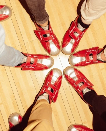 Overhead shot of six people wearing red and silver bowling shoes standing in a circle on a wood bowling alley floor.