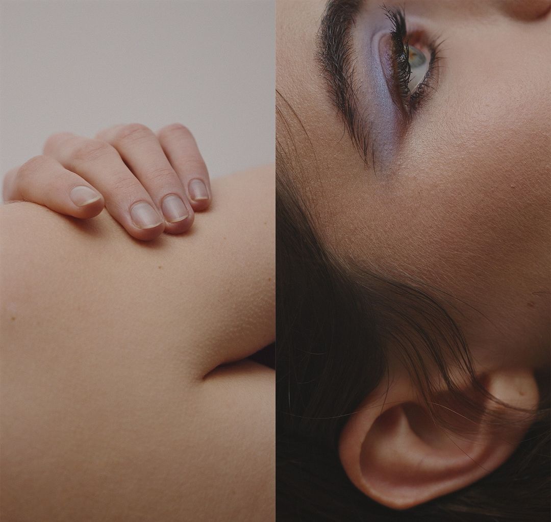 Closeup studio shot of a woman's face with blue eyeshadow, paired with a hand resting on skin, creating a minimalist beauty composition.