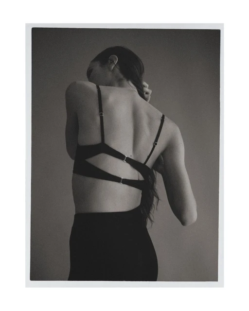 Back view of a woman with braided hair wearing a black bralette and skirt against a neutral gray background in a minimalist style.