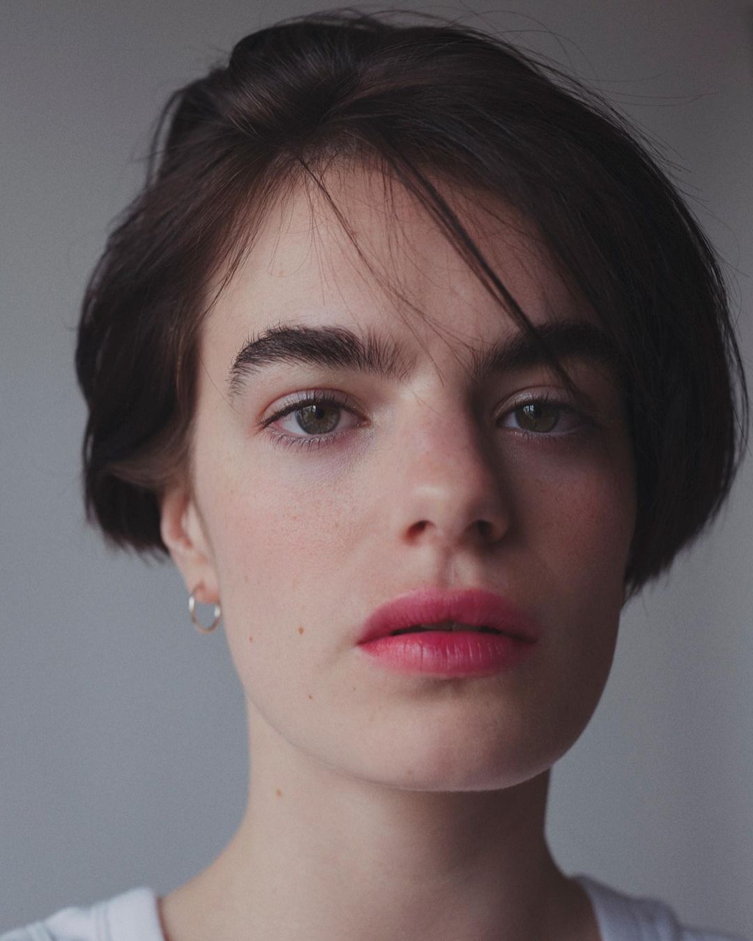 Close-up portrait of a woman with short dark hair and pink lipstick wearing a silver hoop earring, by Guillaume Millet