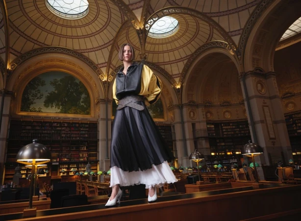 Adult woman in modern layered fashion posing in grand library interior with books, architectural details, and ambient light.