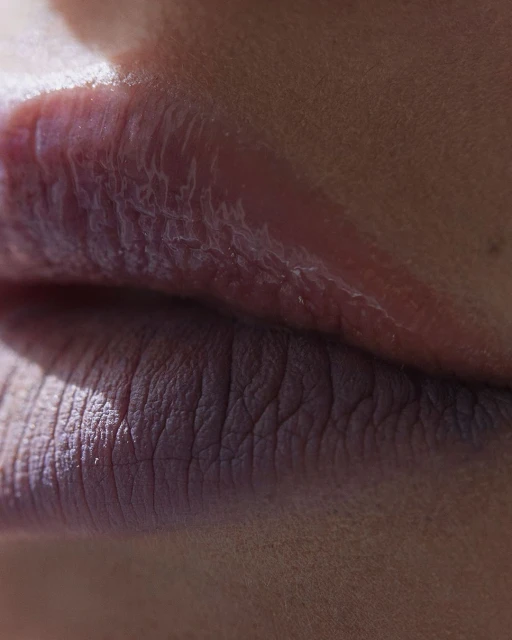 Close-up photograph features an adult female's lower face, focusing on her lips, which are textured, reflecting light, and in focus.