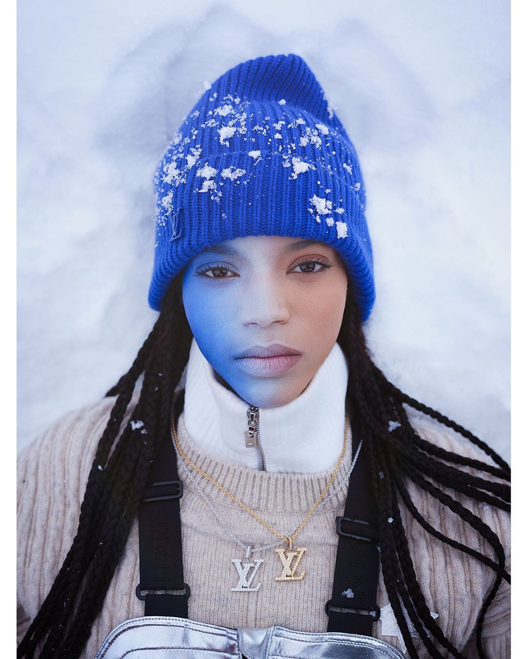 Close-up of a young woman with blue hat in snowy setting. The person has Louis Vuitton branded jewelry and outfit.