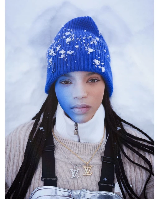 Close-up of a young woman with blue hat in snowy setting. The person has Louis Vuitton branded jewelry and outfit.