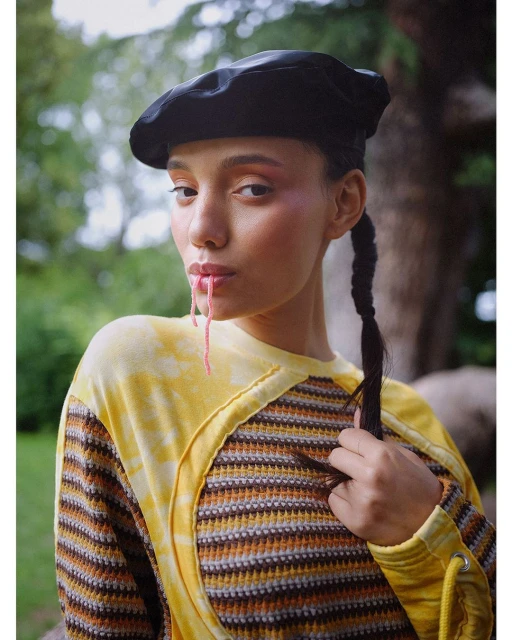 Close-up portrait of a young woman wearing a black beret and striped yellow top, posing in a natural outdoor setting.