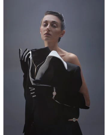 Portrait of a woman in a black and white dress with white gloves looking at the camera in a studio with a grey background.