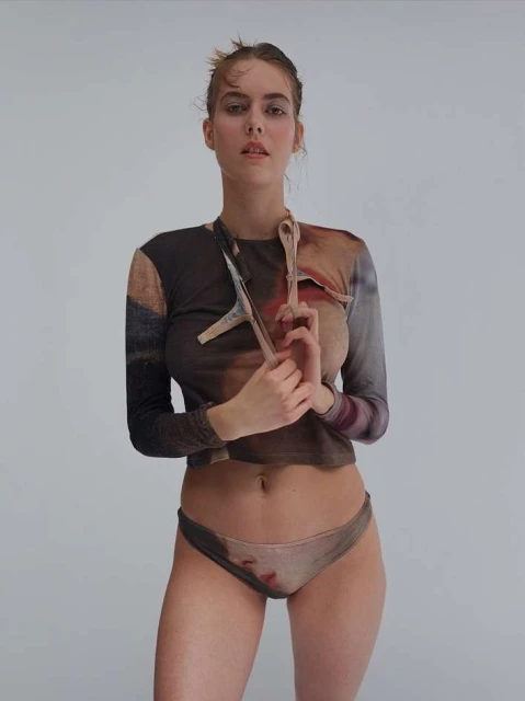 Young woman in printed long-sleeve shirt and briefs, posing in a full shot against a neutral backdrop in a studio setting.