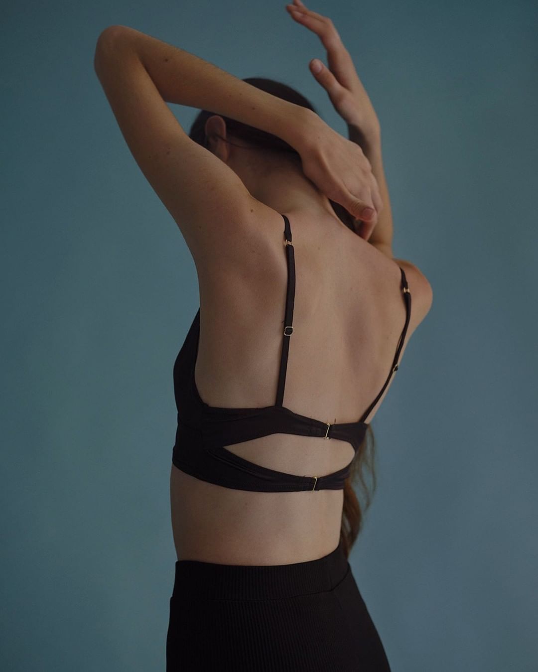 Woman in black bra and leggings poses with arms raised against a blue background, showcasing an active and fashionable lifestyle.