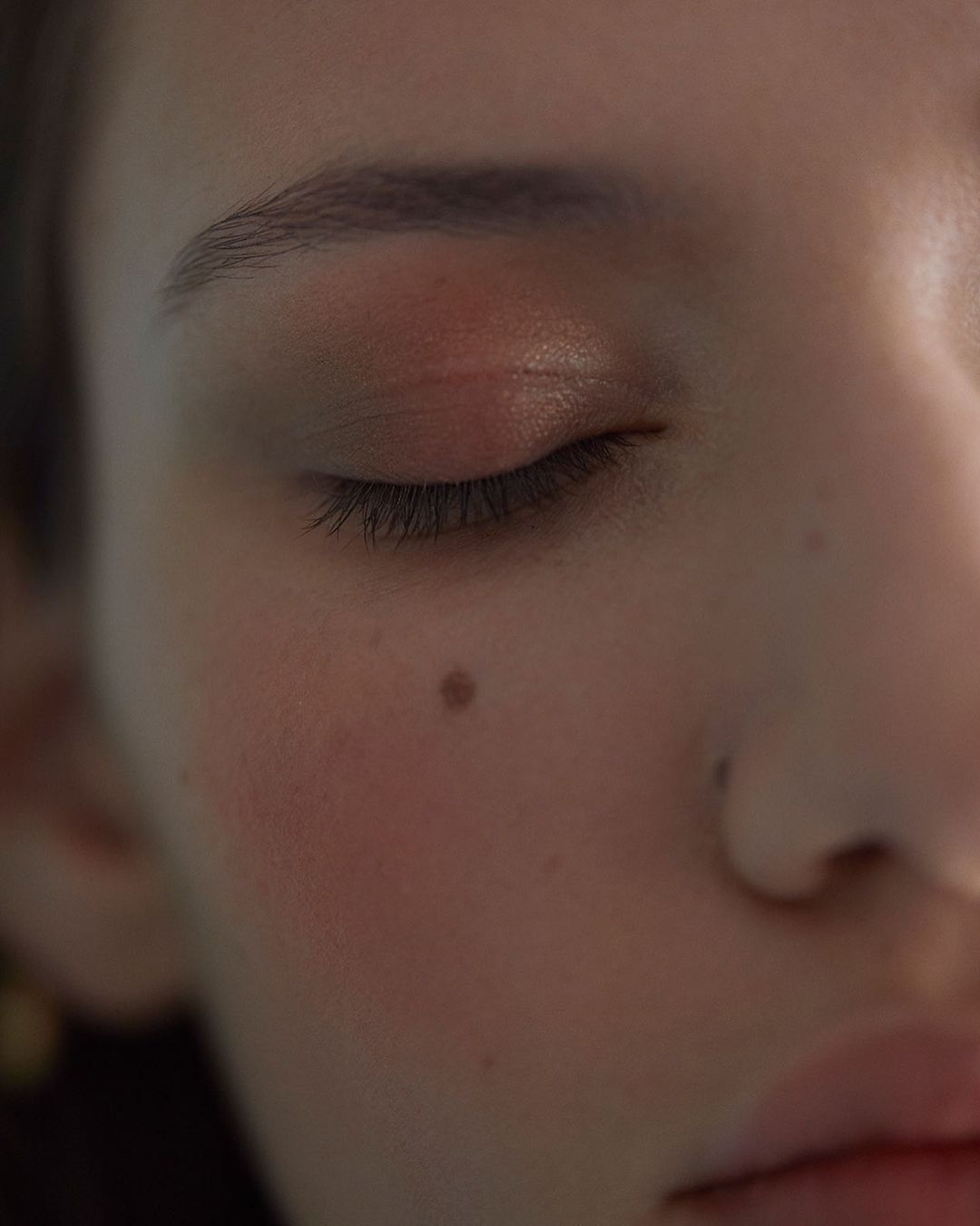 Close-up portrait of a woman with closed eyes, soft lighting, and a distinct mole on her cheek, photographed by Guillaume Millet
