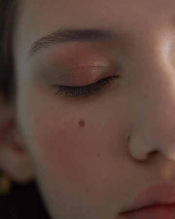Close-up portrait of a woman with closed eyes, soft lighting, and a distinct mole on her cheek, photographed by Guillaume Millet