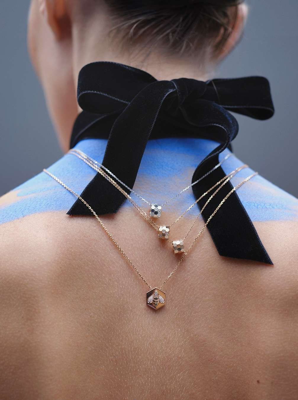 Back view of a fair-skinned adult woman with an ornate black velvet ribbon and three necklaces in a vertical, indoor shot.