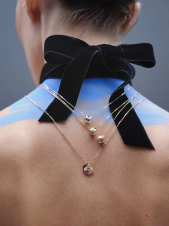 Back view of a fair-skinned adult woman with an ornate black velvet ribbon and three necklaces in a vertical, indoor shot.