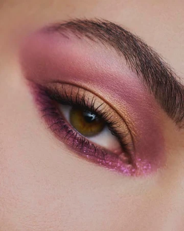 Extreme close-up of a brown eye featuring vibrant pink eyeshadow, gold shimmer, and dark mascara by Gus & Lo.