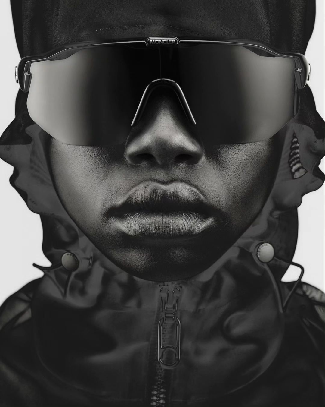 Close-up of a person wearing sunglasses and a hooded jacket, creating a monochromatic portrait in dark tones against a light background.