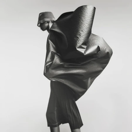 Model wearing a bucket hat and sculptural metallic cape against a light background, photographed by Gus and Lo