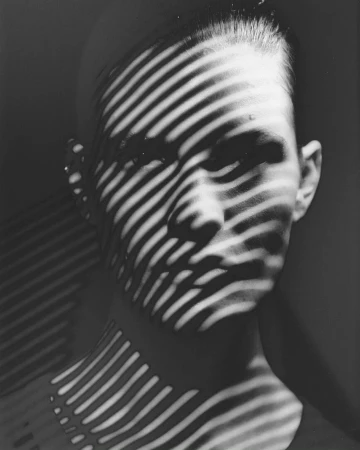 Close-up black and white portrait of a person's face with dramatic striped shadow patterns cast across it.