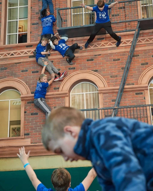 Group of children in blue shirts on a brick facade with windows and balconies, creating a playful and dynamic scene.
