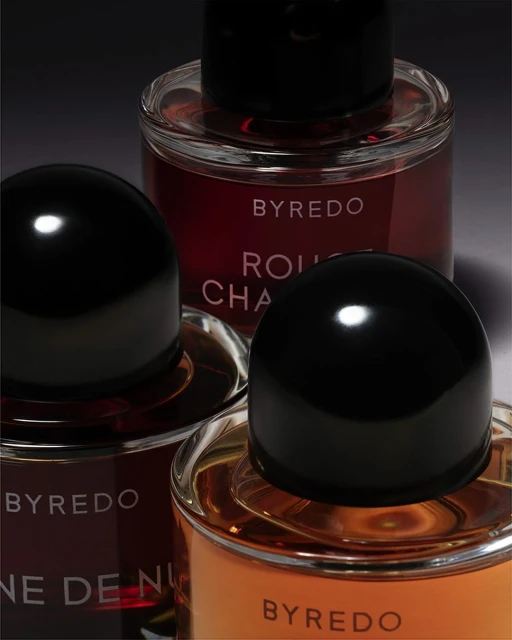 Close-up of three Byredo fragrance bottles with black caps: 'Rouge Chaotique', 'Reine de Nuit', and amber liquid perfume.