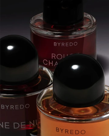 Close-up of three Byredo fragrance bottles with black caps: 'Rouge Chaotique', 'Reine de Nuit', and amber liquid perfume.