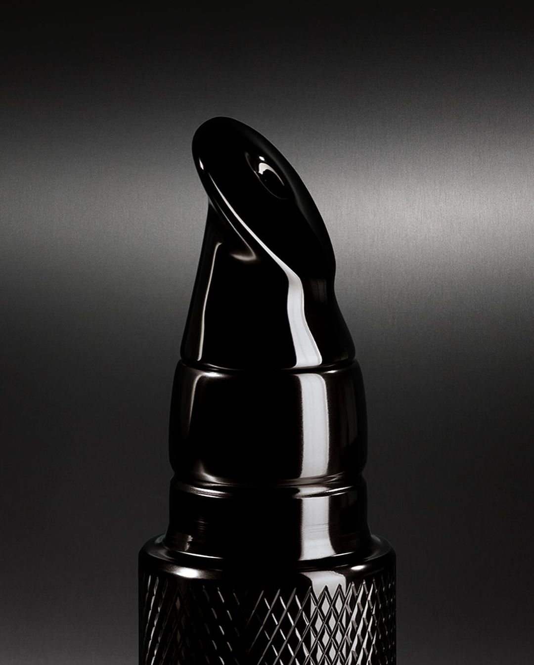 Close-up of a sleek black bottle with a unique applicator, set against a dark gray background, highlighting its glossy texture.