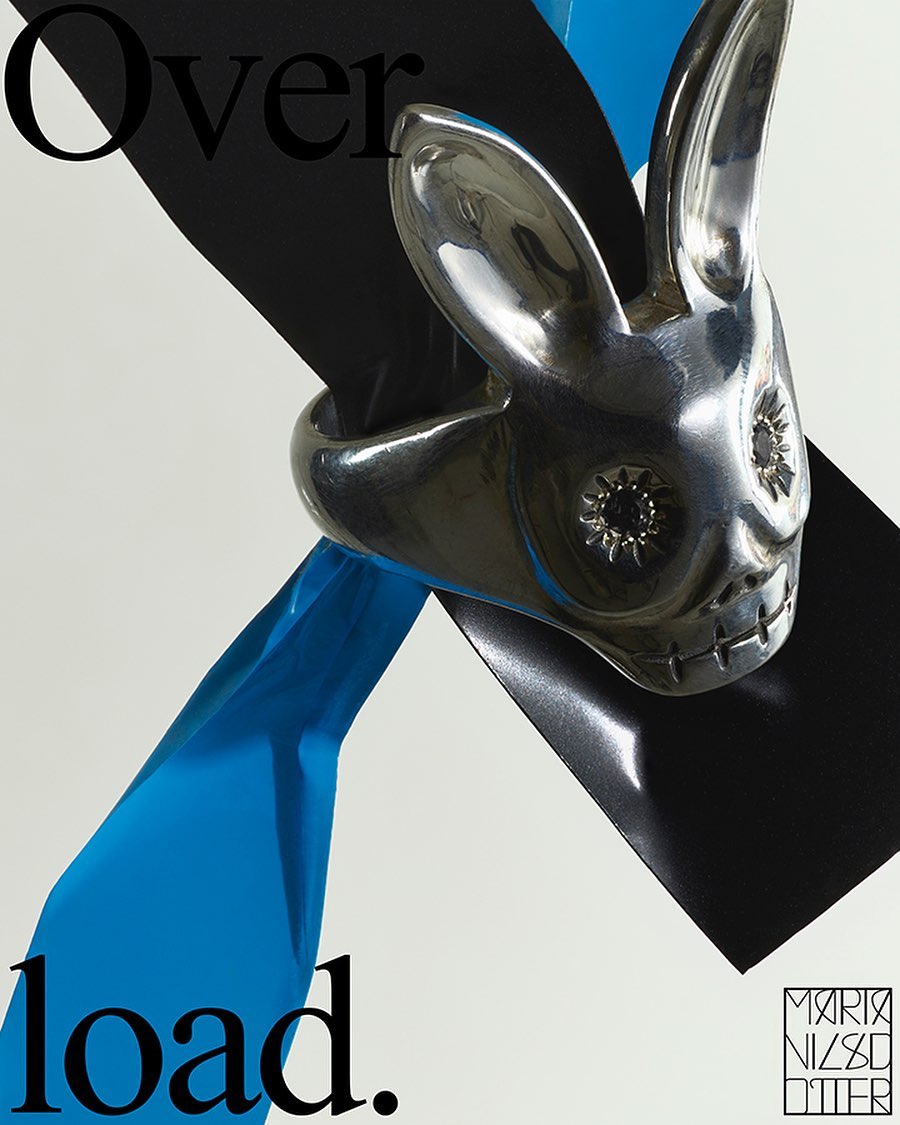Silver rabbit ring showcased on a white backdrop with a black square and a blue ribbon; contemporary jewelry advertisement.