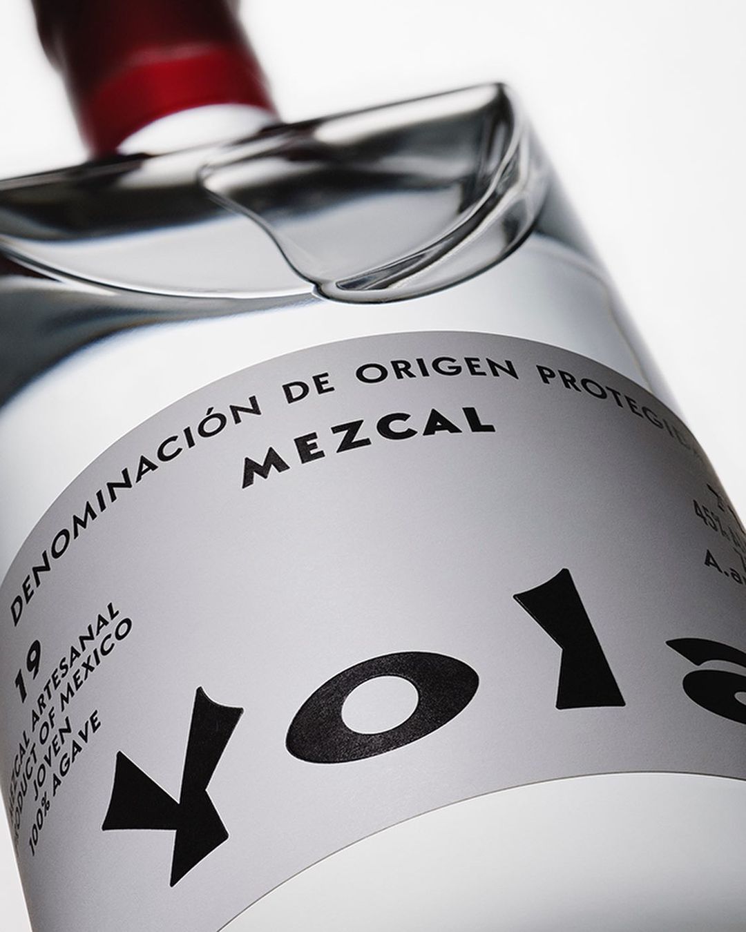 Close-up of a clear glass mezcal bottle with a white label and black text, featuring the brand name 'Volans' prominently.