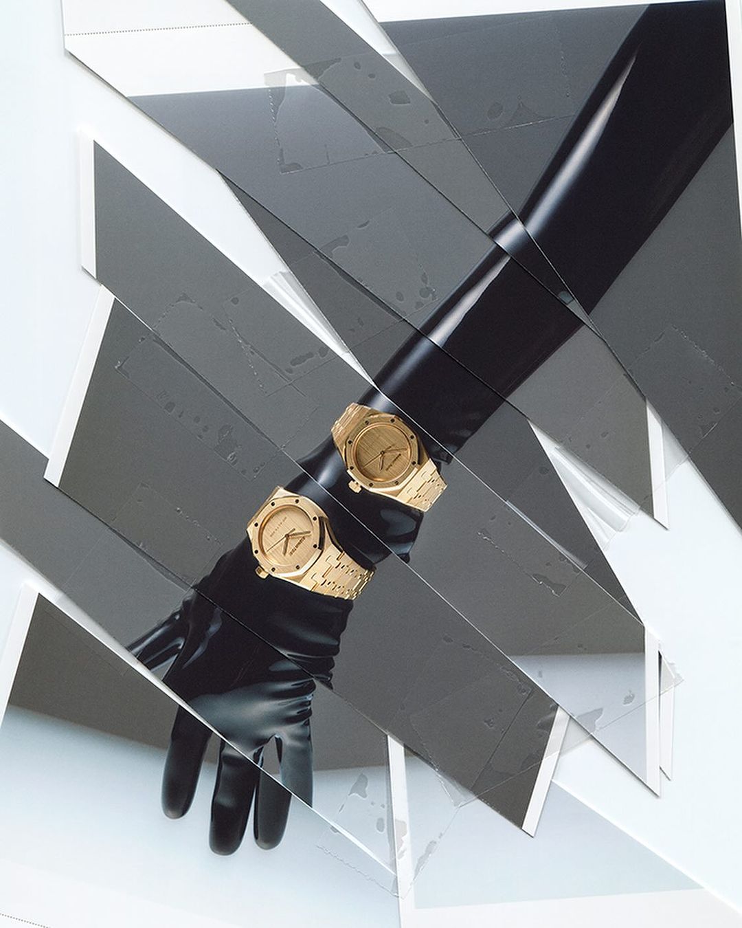 Two golden watches are elegantly displayed on a black gloved arm, set against an avant-garde background of white and grey fragmented shapes.