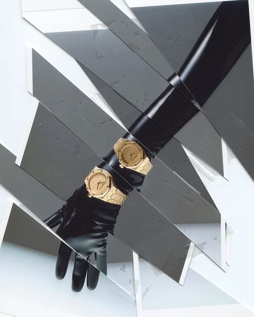 Two golden watches are elegantly displayed on a black gloved arm, set against an avant-garde background of white and grey fragmented shapes.