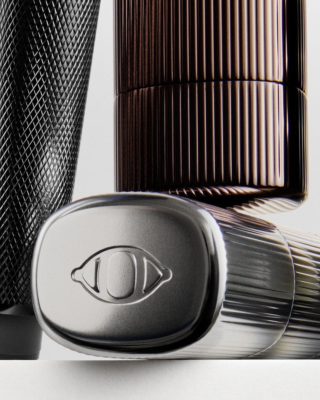 Still life photograph of silver and brown cosmetic containers with various textures, set against a plain white background.