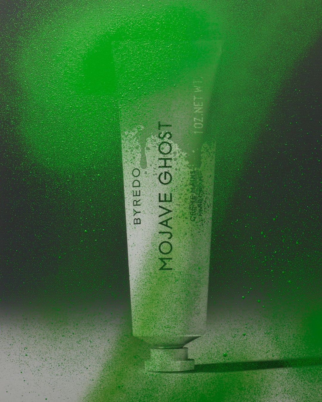 Byredo Mojave Ghost hand cream tube against a backdrop with a gradient of green spray paint. Beauty product, skincare, hand care.
