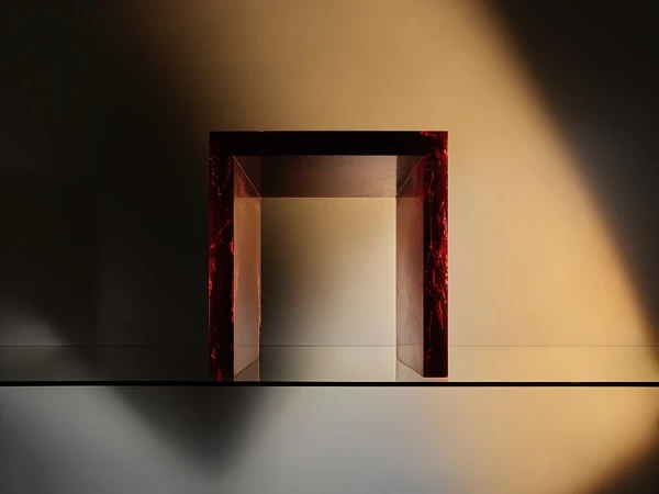 A modern display featuring a unique U-shaped object with a red marble-like finish, showcased on a reflective glass surface against a gradient backdrop.