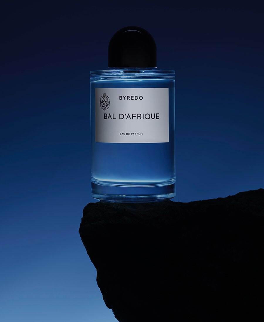 Byredo Bal d'Afrique perfume bottle displayed on a rock formation against a gradient blue background in a beauty still-life shot.