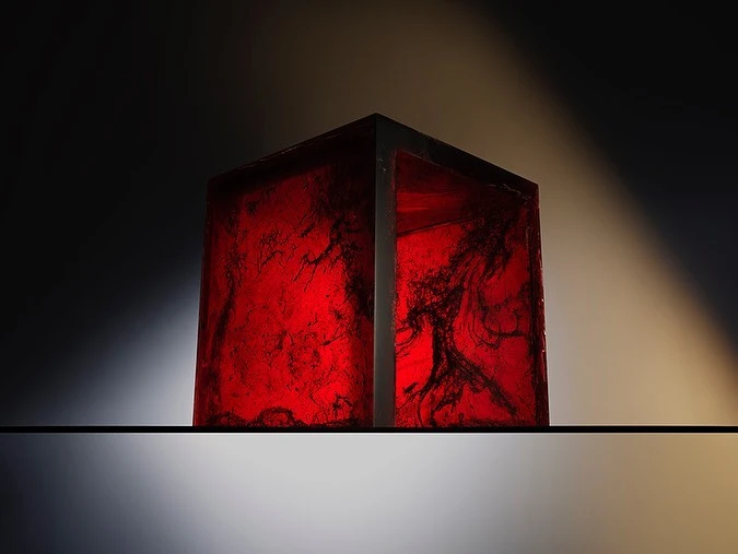 Abstract shot of a translucent red cube with black marbling resting on a reflective surface against a dark background with subtle spotlighting.