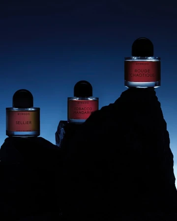 Three perfume bottles positioned on jagged dark rock formations against a deep blue gradient background.