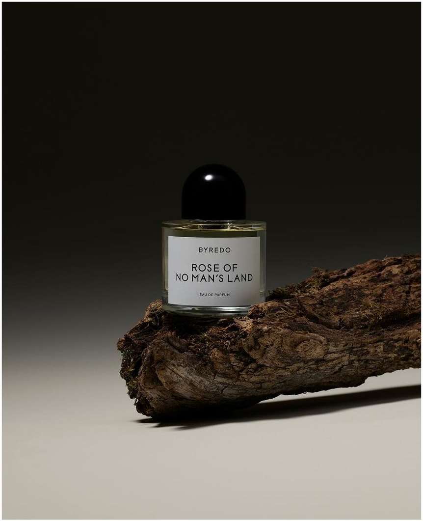 Still life studio shot of a Byredo perfume bottle on a piece of wood against a dark background, product photography, beauty, fragrance.