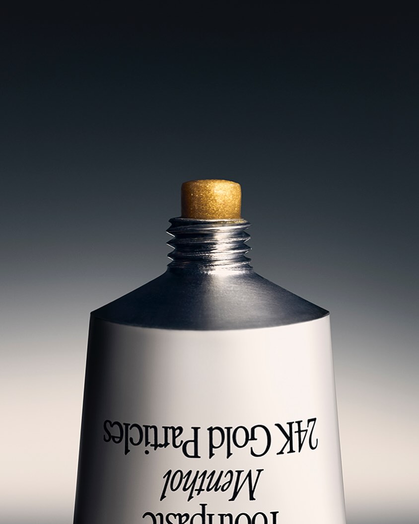 Close-up studio shot of a white toothpaste tube with a gold cap, showcasing product details against a gray gradient background.