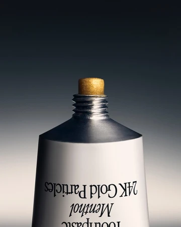 Close-up studio shot of a white toothpaste tube with a gold cap, showcasing product details against a gray gradient background.